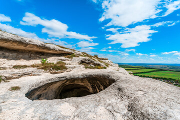 Panoramic view of huge hole in ground among green field and mountain on sunny summer day in Crimea. Abnormal cave, failure in ground. Anomaly grotto.
