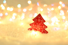 A Red Wooden Christmas Tree With White Patterns In The Snow Against A Background Of Bright Lights. Christmas Atmosphere. Space For Text. Minimalism.