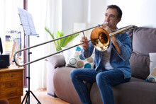 Man Practicing Trombone With Enthusiasm In Living Room At Home