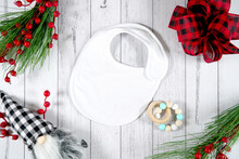 Baby Bib Product Mockup. Christmas Farmhouse Theme SVG Craft Product Mockup Styled With Gift With Buffalo Plaid Bow And Farmhouse Style Gnomes Against A White Wood Background.