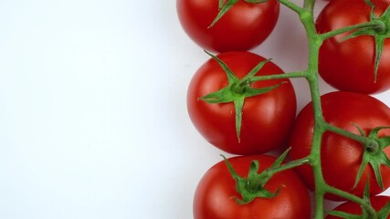 Wall Mural - Branch cherry tomatoes rotate on a white plate background, top view close-up