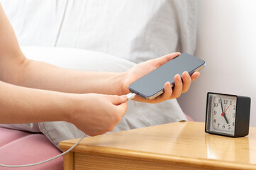 Woman hands plugging a charger in a smart phone in the bedroom at home