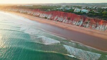 Scenic Aerial View Of Red Rocky Cliffs Of Praia Da Falésia, Vilamoura, Algarve. Portugal Sandy Beach With Luxury Houses From Above By Red Rocks Seashore With Smooth Sea Waves During Sunset In 4K.