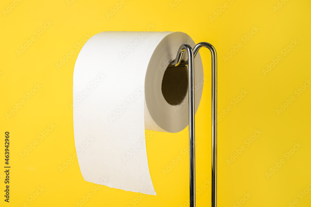 Holder with toilet paper roll on yellow background, closeup