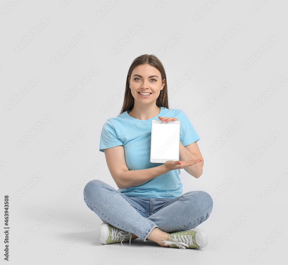 Pretty young woman with tablet computer on light background