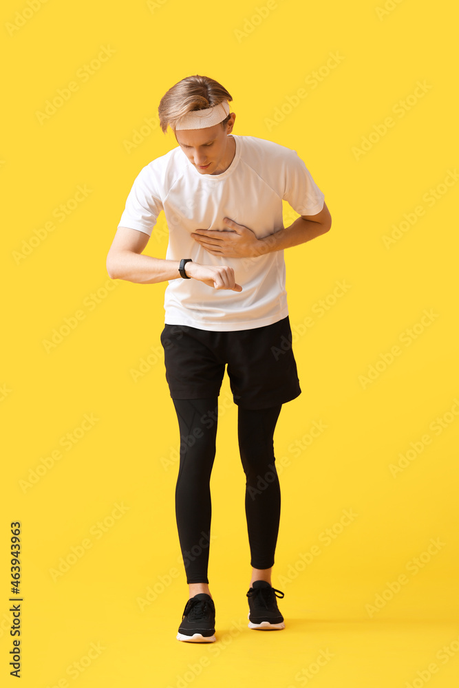 Sporty male runner checking pulse on color background