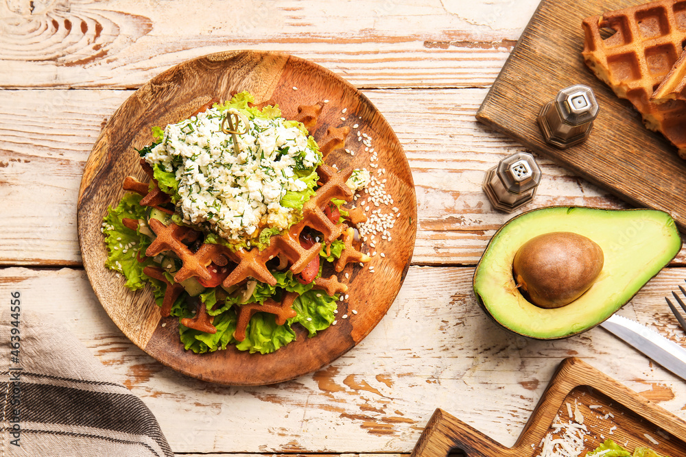 Plate with delicious Belgian waffles and vegetables on light wooden background