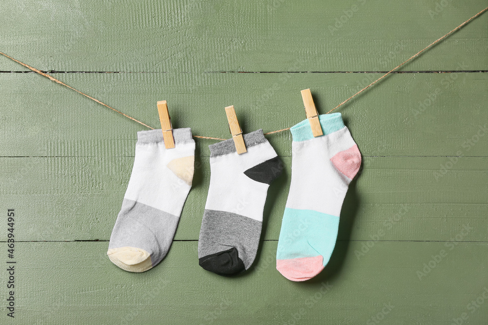 Different socks hanging on rope against green wooden background