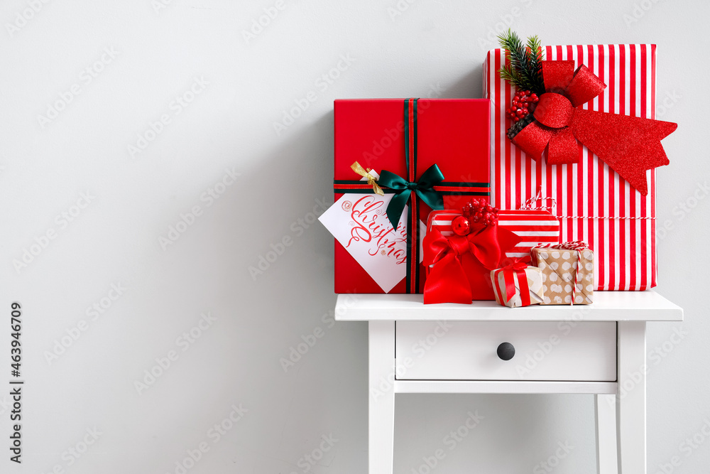 Beautiful Christmas gifts on table near light wall