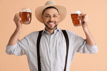 Young man in traditional German clothes with beer on beige background