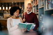 © Drazen - Black woman and her mature friend studying from book during research in a library.
