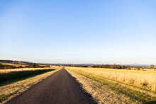 Unmarked Rural Country Road Through Paddocks Of Long Brown Grass