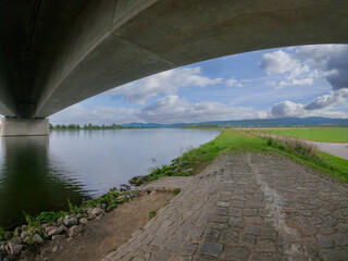 Canvas Print - Landscape of unpaved road under a bridge near the river