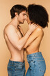 © LIGHTFIELD STUDIOS - side view of shirtless man and topless hispanic woman embracing while smiling at each other isolated on beige.