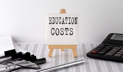 Aufkleber - text EDUCATION COSTS on easel with office tools and paper.Top view. Business concept