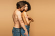 sexy man in jeans hugging latin woman hiding breast with crossed arms isolated on beige.
