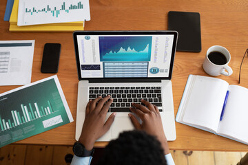 Hands of african american businessman sitting at desk, using laptop with statistical data on screen