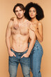 © LIGHTFIELD STUDIOS - shirtless man standing with hands in pockets of jeans near sexy hispanic woman embracing him isolated on beige.