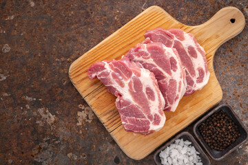 raw pork chop fillet in wooden cutting board with salt and pepper on rusty texture background with copy space for text, top view, flat lay