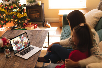 Caucasian mother and daughter making laptop christmas video call with diverse friends and family