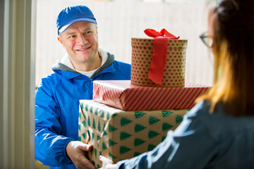 Delivery man bringing holiday packages. Woman at home standing in doorway, receiving parcels for Christmas gifts. 