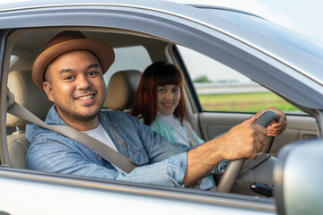 Happy two young friends driver smiling while sitting in a car with open front window. Asian man and woman smile and looking through window. Young couple driving car to travel on holiday vacation time.