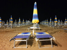 An Empty Beach At Night With Blue And Yellow Umbrellas And Sun Loungers.