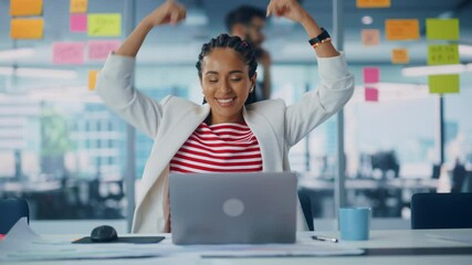 Poster - Young Successful Black Project Manager Dances and Smiles While Sitting at Her Desk. Beautiful Female Specialist Works on Laptop Computer in Creative Office, Celebrates Successful e-Commerce Project