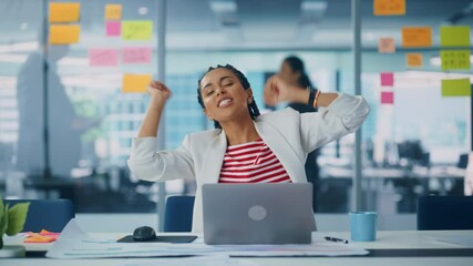 Poster - Young Successful Black Businesswoman Dances and Smiles While Sitting at Her Desk. Beautiful Female Specialist Works on Laptop Computer in Creative Office, Celebrates Successful e-Commerce Project