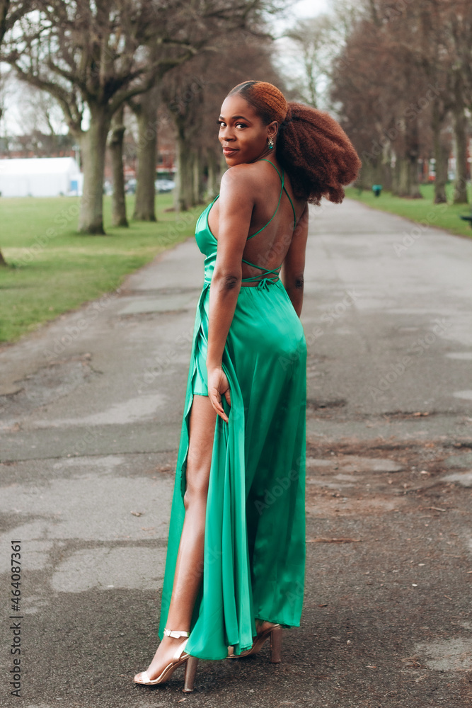 princess polly baby blue dress Beautiful African black woman walking in park in autumn. Beautiful young  woman with brown skin. Smiling black woman with afro hair wearing green  dress with high slit. Stock Photo