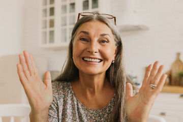 Wall Mural - Pretty attractive 60-years-old female blogger with natural make-up, grey hair, glasses on head gesticulating with wide smile, telling story of her life and success. People, online business, blogging