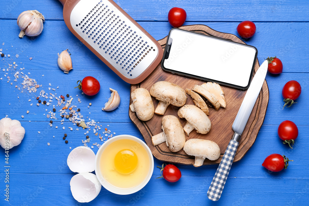 Mobile phone, kitchen utensils and different ingredients on color wooden background