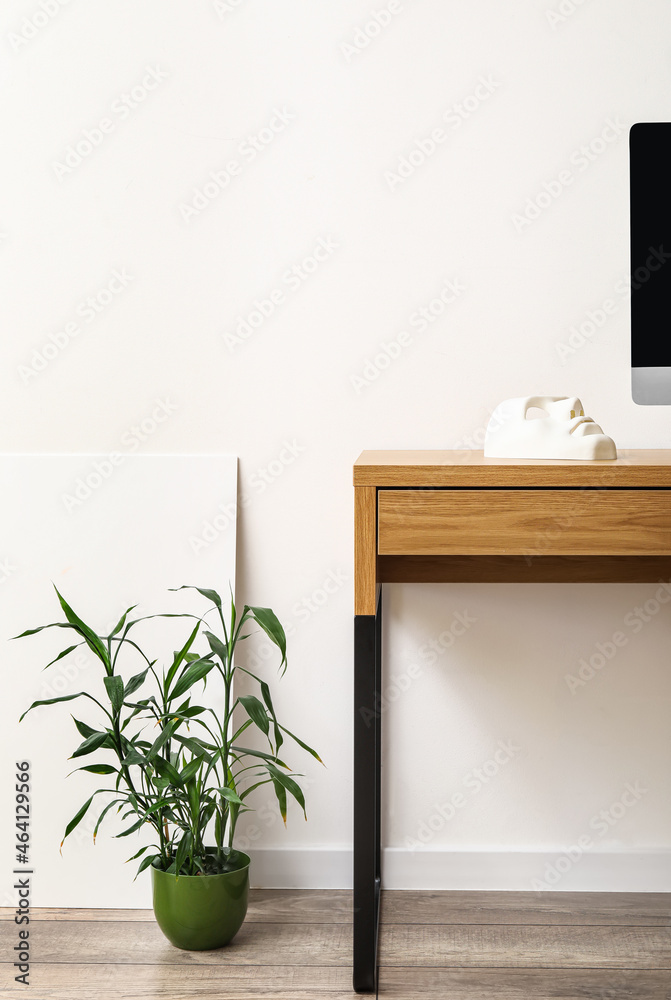 Wooden table with houseplant near light wall