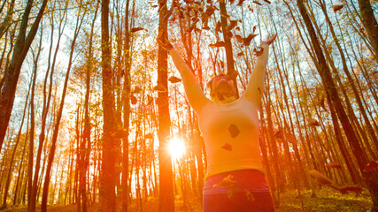 Wall Mural - CLOSE UP: Female hiker plays with the crunchy fallen leaves on sunny evening.