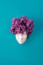 Plaster Face, Figurine Decorated With Lilac Flowers. Lilac As A Hairstyle On The Head Figurine Against Blue Background. Flat Lay Floral Composition.