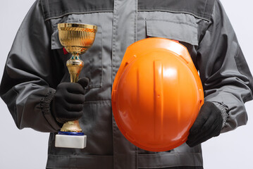 builder contractor with a gpolden award trophy and hardhat in hands close up.