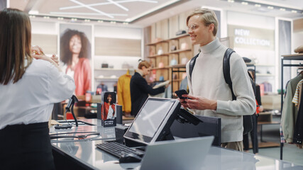 Wall Mural - Clothing Store: Young Man At Checkout Counter Buys Clothes Paying with Contactless NFC Smartphone, Friendly Retail Sales Assistan Packs Merchandise. Contemporary Fashion Shop with of Designer Brand