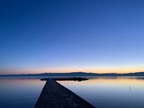 Fototapeta Pomosty - Silhouette of a long pier at the surface of the lake, sunset time, natural colors