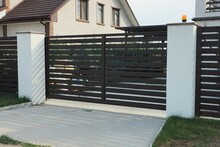 One Closed Black Wooden Gate And Part Of A Fence Wall Made Of White Concrete Pillars And Planks Outside