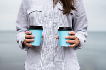 Woman holding in hands a coffee cups on a blue sea water background.