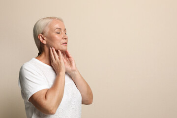 Wall Mural - Mature woman doing thyroid self examination on beige background, space for text