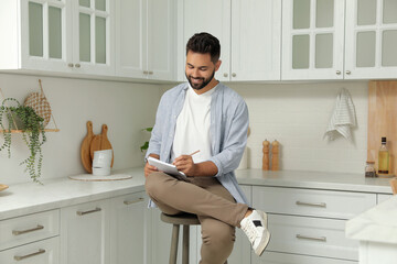 Wall Mural - Handsome young man with notebook sitting on stool in kitchen