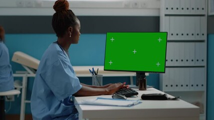 Nurse working with keyboard and horizontal green screen on computer at desk. Healthcare specialist using monitor with modern technology for isolated template and mockup background.
