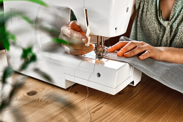 Seamstress sewing the linen fabric on the sewing machine in small studio. Fashion atelier, tailoring, handmade clothes concept. Slow Fashion Conscious consumption