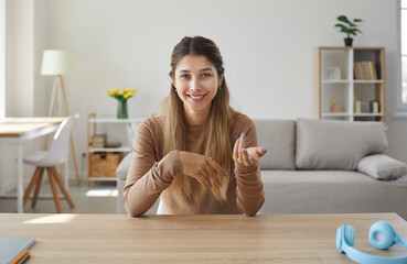 Laptop computer screen view of happy beautiful young woman sitting at work desk in home office in living room, gesturing and talking to friend or colleague during casual online meeting via video call