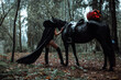 mask in the form of a pumpkin with burning eyes. creepy girl costume for halloween. a rider in a long black cloak holds a horse by the bridle. cosplay of a gloomy image in the autumn forest