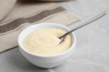 Bowl with gelatin powder and spoon on light grey marble table, closeup