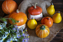 Pumpkins And A Bouquet Of Wildflowers Lie On Rough Burlap On A Wooden Background.