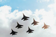 A squadron of jet soldiers, fighters, and airplanes perform a maneuver against the background of a blue and cloudy sky.