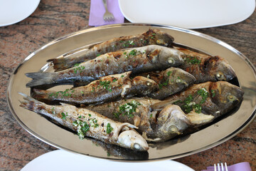 Canvas Print - Top view shot of grilled sea fish in an oval metal plate on the table at a restaurant